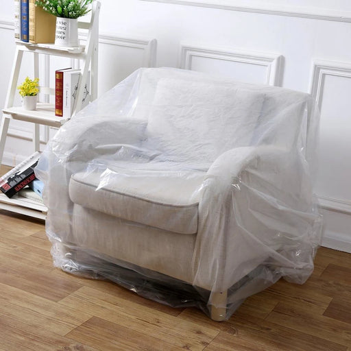 White armchair covered with clear armchair cover bag in a room with wooden floor and white walls.