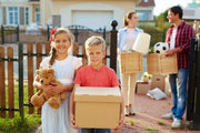 two young children with their parents holding cardboard boxes in from of their new home