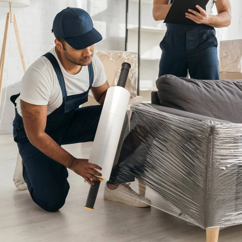 A man wrapping a fabric sofa with clear pallet wrap in an empty living room