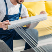 Man in blue overalls wrapping a sofa in clear pallet wrap