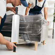 Two people wrapping a sofa with clear pallet wrap in an empty living room.