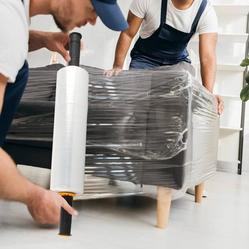Two people wrapping a sofa with clear pallet wrap in an empty living room.