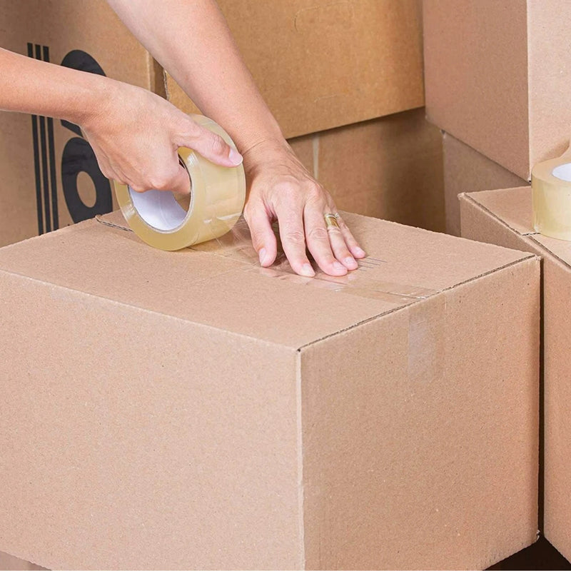 Person taping a cardboard box with clear sealing tape surrounded by moving boxes
