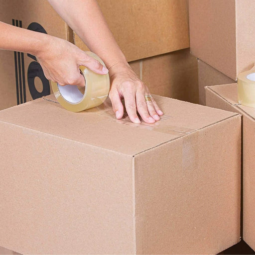 Person taping a cardboard box with clear sealing tape surrounded by moving boxes