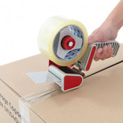 Person using a tape gun to seal a cardboard box with clear sealing tape on a white background