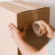 closeup of a person sealing a cardboard box with clear tape
