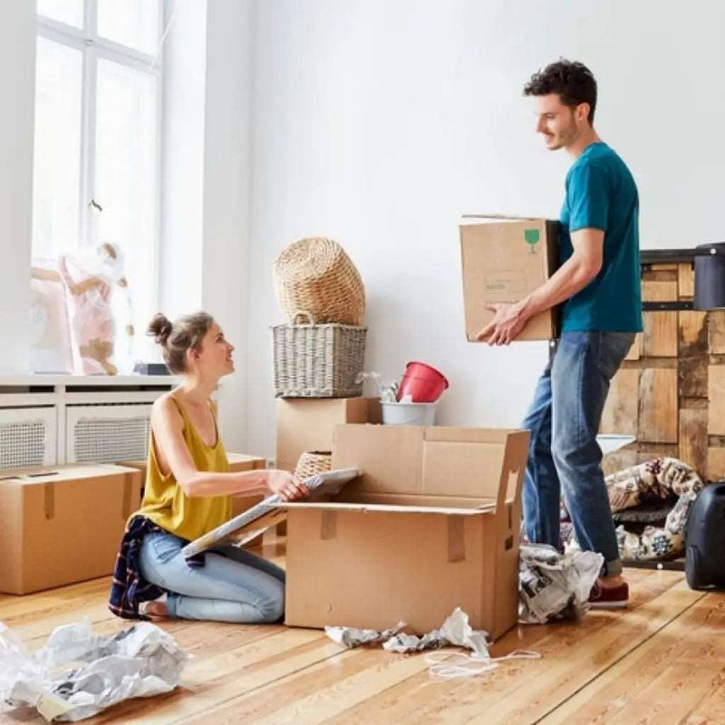 a couple packing up their living room belongings into cardboard boxes