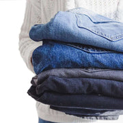 woman holding a folded pile of denim jeans suggesting that she is decluttering
