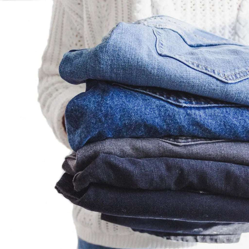 woman holding a folded pile of denim jeans suggesting that she is decluttering