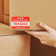 Hand holding a cardboard box with a fragile label stuck to the box
