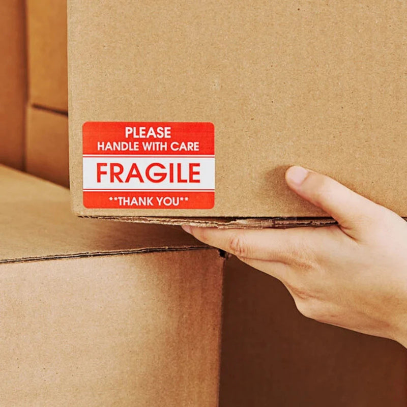 Hand holding a cardboard box with a fragile label stuck to the box