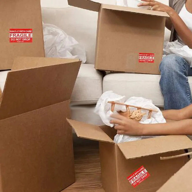 Person unpacking items from cardboard boxes with 'Fragile' labels on the boxes while sitting on a couch.