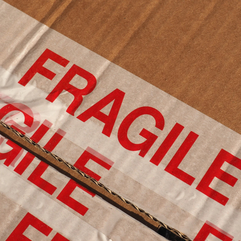 closeup of a cardboard box that was sealed with multiple layers of fragile tape but has now been opened