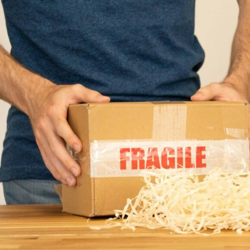 man holding a cardboard box sealed with  fragile tape on a wooden desk