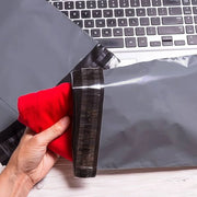 a hand placing clothing into a grey mailing bag at a desk with a computer in the background