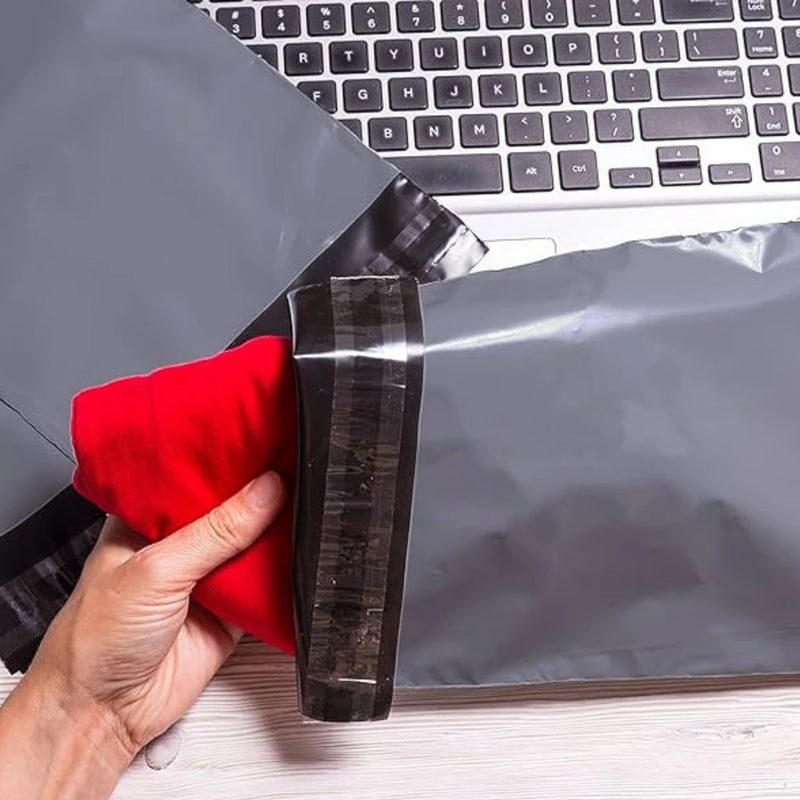 a hand placing clothing into a grey mailing bag at a desk with a computer in the background