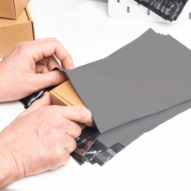 a man placing a small cardboard box into a grey mailing bag at a desk