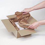 Hands putting paper voidfill into a cardboard box on a white background