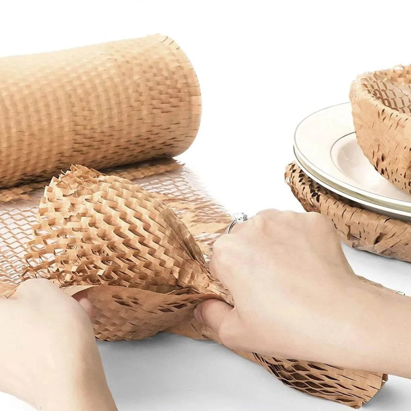 a hand wrapping plates, bowls and glasses in protective honeycomb paper on a white background