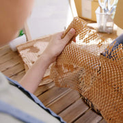 a woman at a wooden desk stretching honeycomb  paper suggesting that she is going to wrap something with it