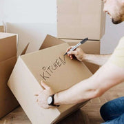 A man using a black marker to label a cardboard box "Kitchen" suggesting that he is moving house