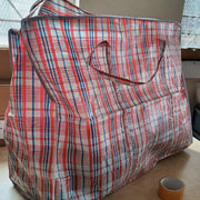 a large tartan coloured plastic storage bag half-filled on a desk with a roll of sealing tape for size perspective