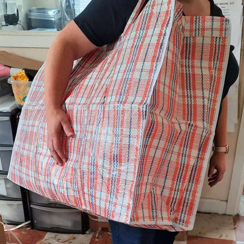 A large tartan plastic storage bag that has been filled and is being worn on the shoulder of a woman