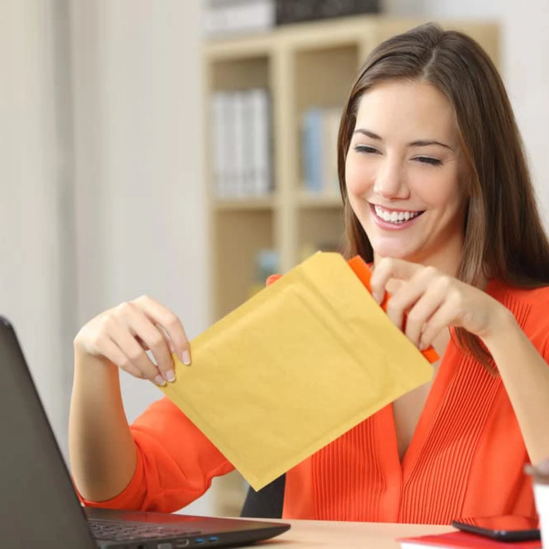 A smiling woman taking a break from working on her laptop to open a brown padded envelope