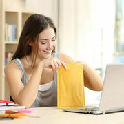 a smiling woman working from home on her laptop opening a brown Mail Lite padded envelope