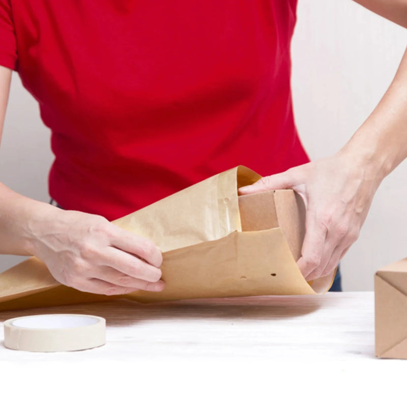 a woman in a red teeshirt packing a cardboard box into a Mail Lite padded envelope