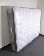 Mattress covered with a clear plastic mattress bag  in an empty room with grey carpet and white walls.