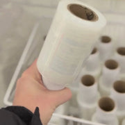 Hand holding a roll of mini pallet wrap with more mini pallet wrap in the background