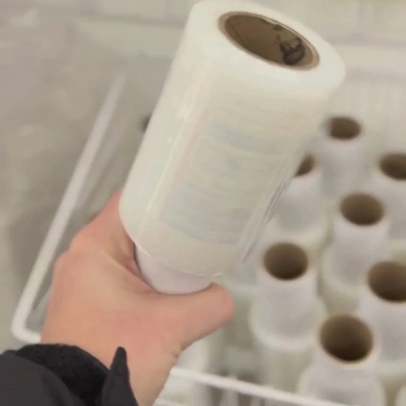 Hand holding a roll of mini pallet wrap with more mini pallet wrap in the background
