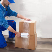 a man kneeling on a wooden floor wrapping two cardboard boxes together using mini pallet wrap