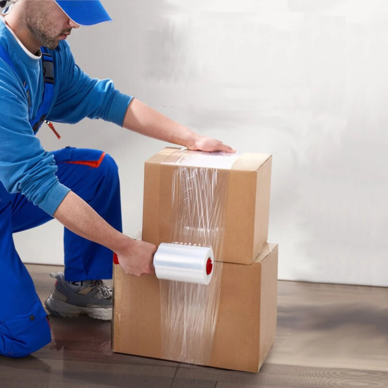 a man kneeling on a wooden floor wrapping two cardboard boxes together using mini pallet wrap