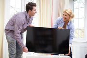 a man and woman lifting a television from a table in preparation for moving house