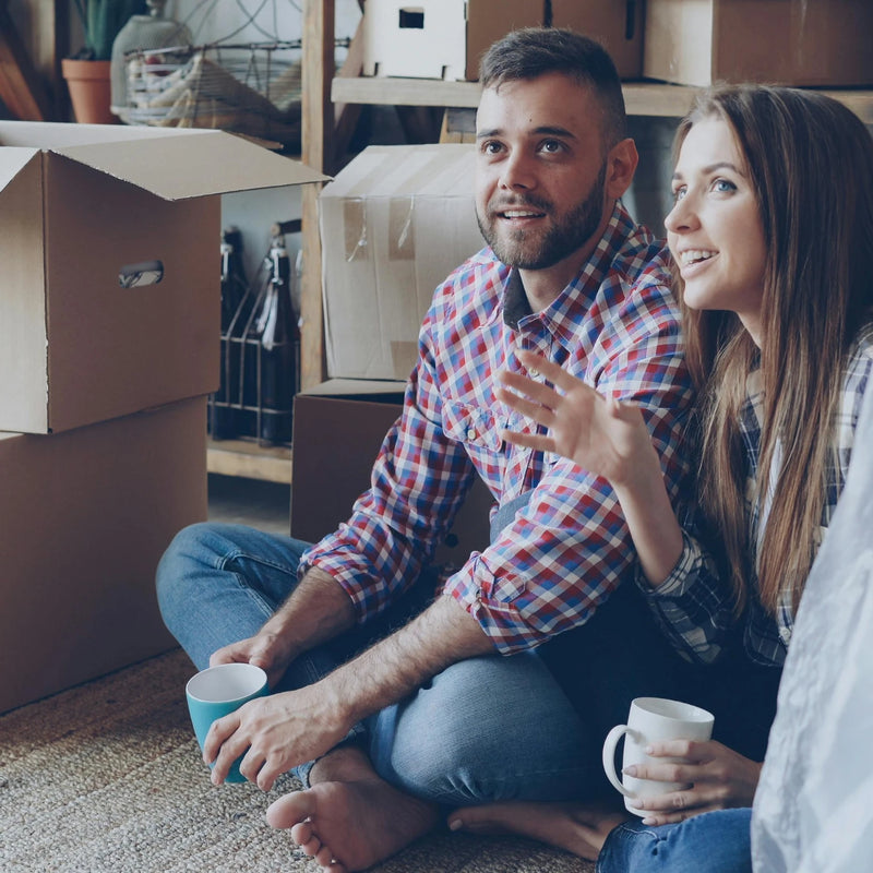 Man and woman sitting on the floor surrounded by moving boxes in a home setting.