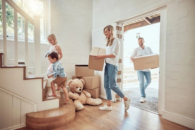 Family with children moving into a new home, carrying cardboard  boxes.