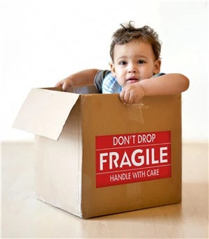 toddler sitting in a cardboard box that has a Fragile Label on the side of it