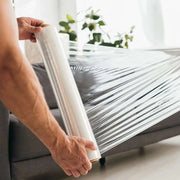 a man preparing to wrap a sofa in clear pallet wrap in an empty living room