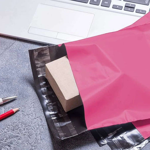 pink poly mailing bags on a desk being filled with products with a laptop in the background