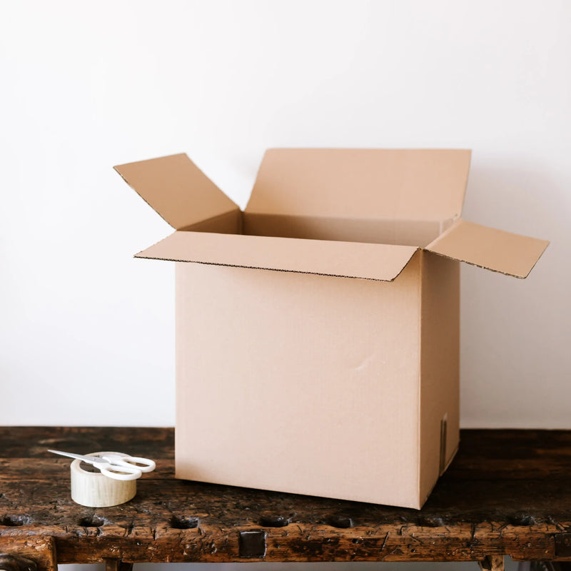 Open cardboard box on a wooden table with a pair of scissors and a roll of clear tape beside it on a white background