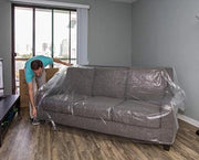 man covering a sofa with a 3-seat sofa cover in an empty living room suggesting that he is moving house