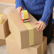 a woman using a tape gun to apply paper tape to a cardboard box