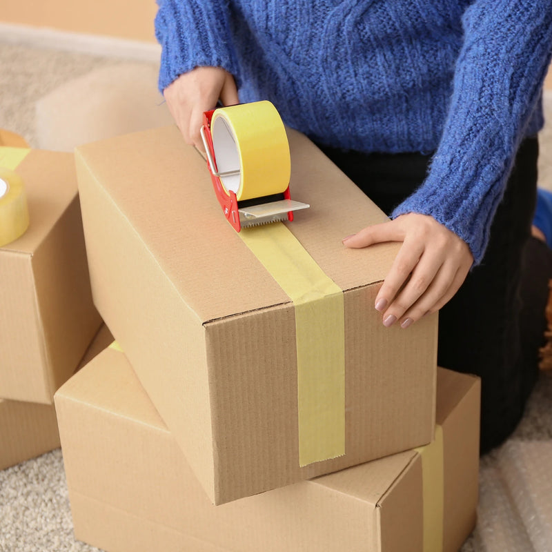 a woman using a tape gun to apply paper tape to a cardboard box