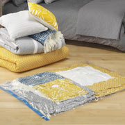 Stack of folded blankets and cushions beside  a vacuum-sealed vacuum storage bag on a wooden floor next to a bed.