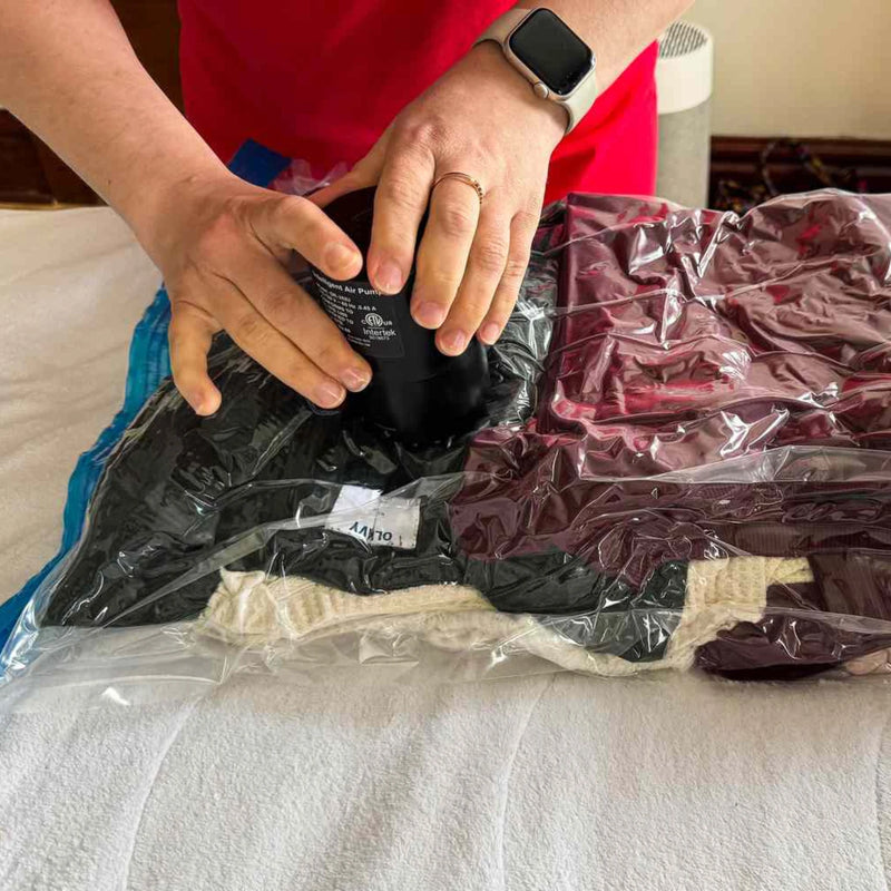 a man using a handheld electric pump to remove air from a vacuum storage bag that is sitting on a bed