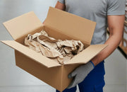 a man holding an open cardboard box filled with paper voidfill in a warehouse environment