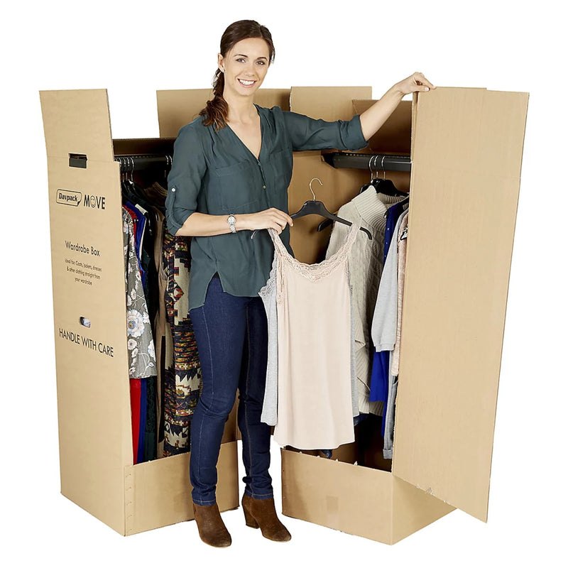 Woman placing clothes on hangars into a cardboard wardrobe moving box on a white background