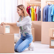 A woman packing up her belongings into cardboard boxes as well as clothing in cardboard wardrobe boxes